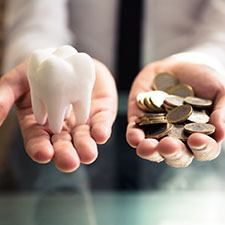 A person holding a white tooth and coins, symbolizing the cost of veneers in Houston