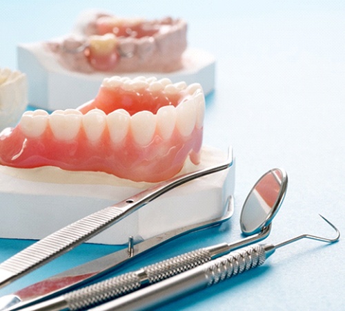 Closeup of full dentures next to dental tools