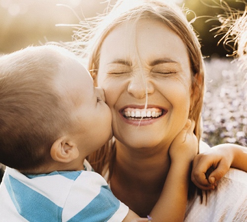 Children kissing their mother as she smiles in preparation for gummy smile correction in Houston