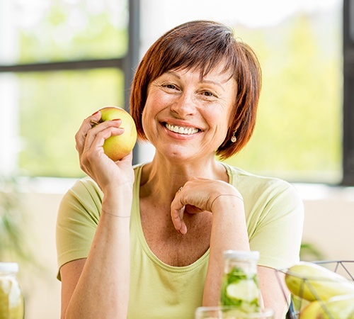 Senior woman eating a green apple after dental implant tooth replacement